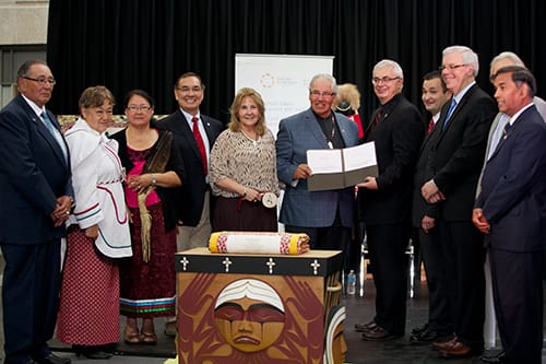 A group of people stand in front of the Bentwood Box, holding the signed Trust Deed.