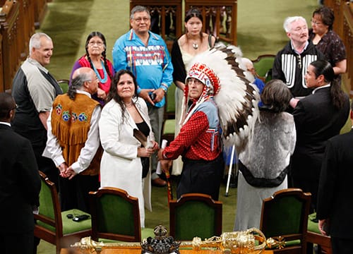 11 Indigenous leaders and Survivors stand in a circle on the floor of Parliament during the Government of Canada apology.