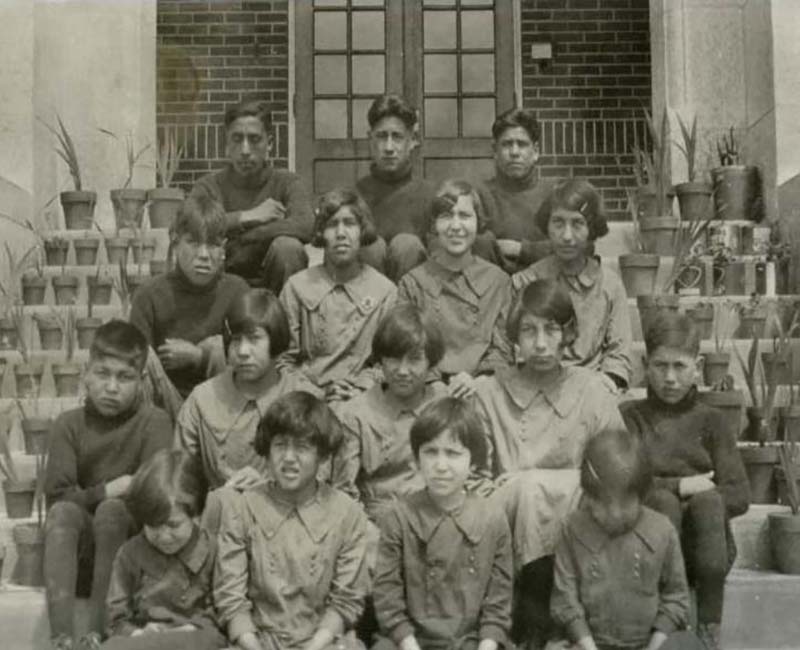 Group of students sitting on steps of building at Muscowequan Touchwood School