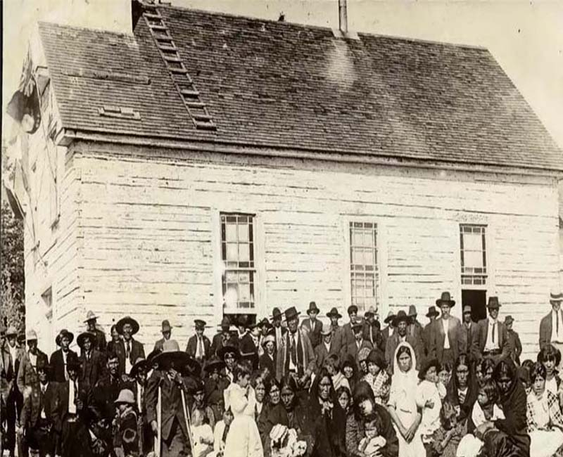 Group of people standing and sitting in front of Cross Lake school building 