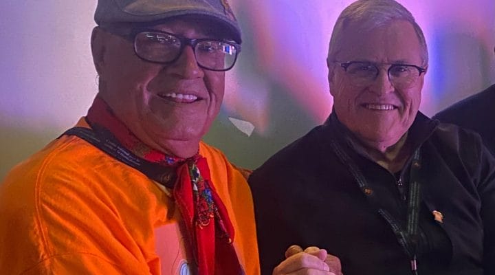 Close-up of Eugene Arcand and Canadian hockey journalist and broadcaster, Bob McKenzie. They are shaking hands and smiling.